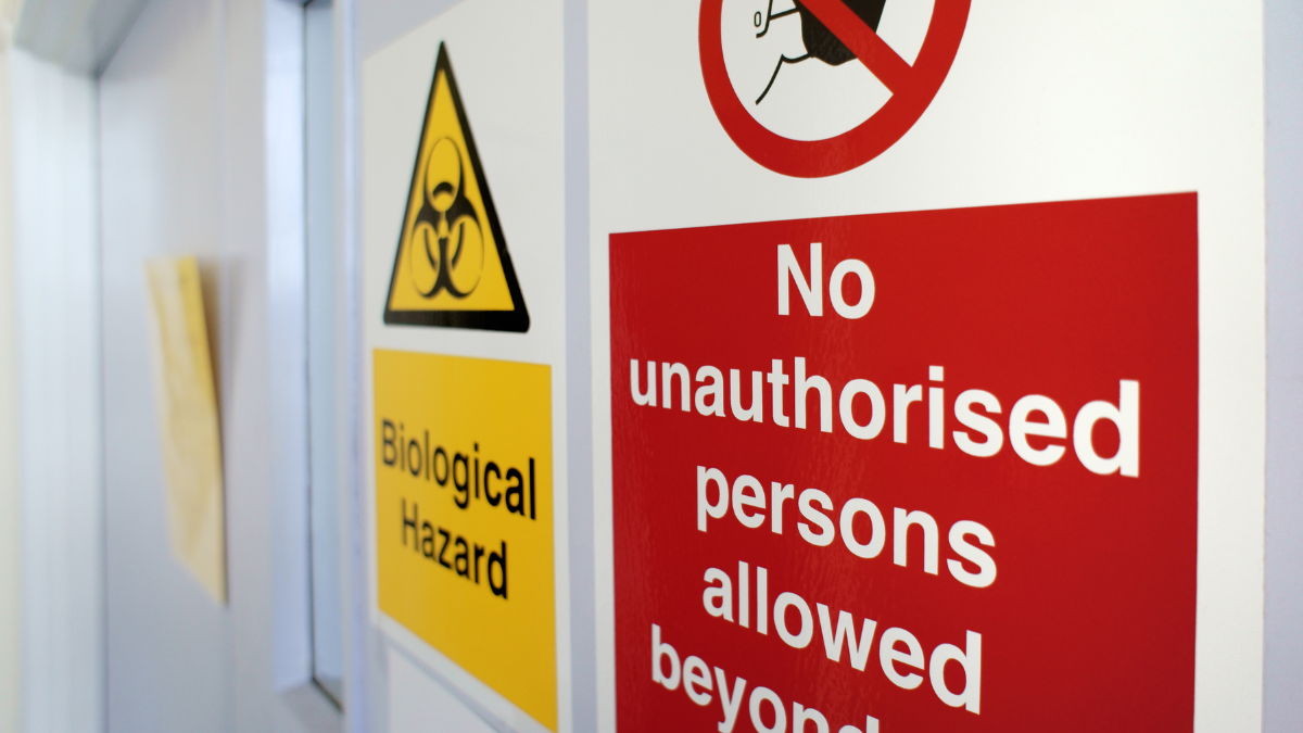 Warning signs indicating a biological hazard and restricting unauthorized access, featuring a yellow biohazard symbol and a red 'No unauthorized persons allowed beyond' notice.